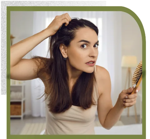 Eine Frau fährt sich durch die Haare und mustert ihr dünnes Haar im Spiegel