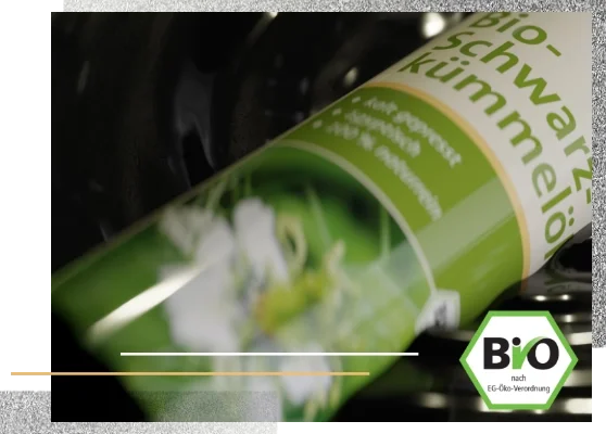 Eine Flasche schwimmt im Öl. Auf dem Produktetikett steht Bio Schwarzkümmelöl Kräuterhaus Sanct Bernhard..