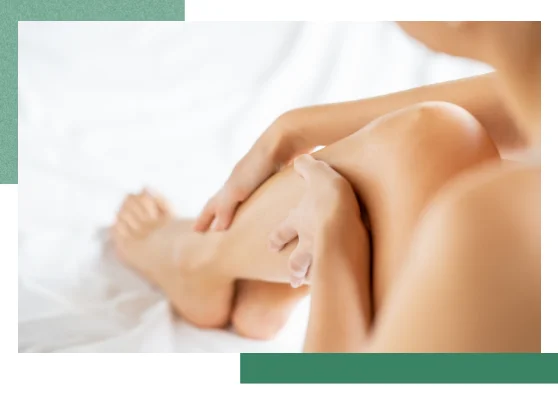 Eine Frau sitzt auf einem Laken und massiert die Waden.