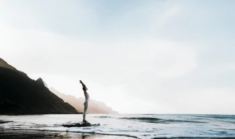 Küstenlandschaft mit einer Frau im linken Bildbereich, die sich in die Luft stretcht.