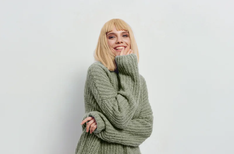 Blonde Frau lächelnd im Wollpullover vor grauem Hintergrund
